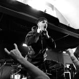 Ung mand, der står på en scene med fingrene til ørene, mens publikum laver metal horn